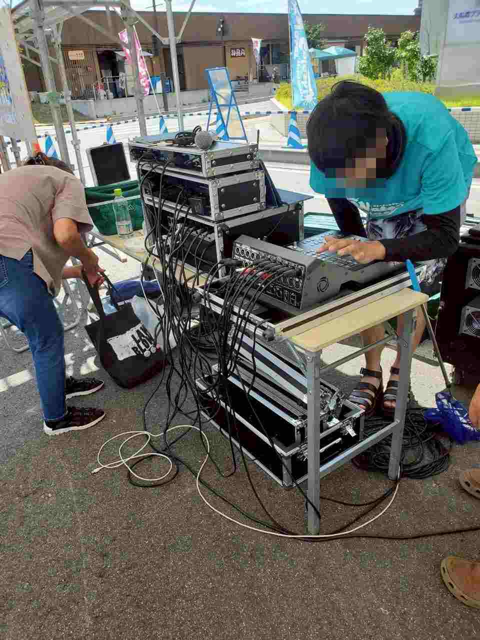 屋外の音響卓とケーブルを調整するスタッフ